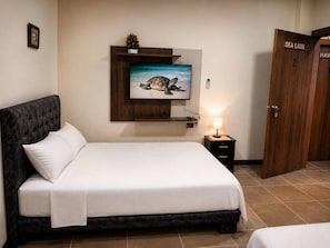Habitación de hotel con una cama, un televisor montado en la pared, una mesita de noche con una lámpara y una puerta de madera con la leyenda 'SEA LION'.