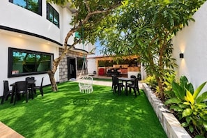 Un patio moderno al aire libre con zona de comedor, una silla blanca y un árbol pequeño.