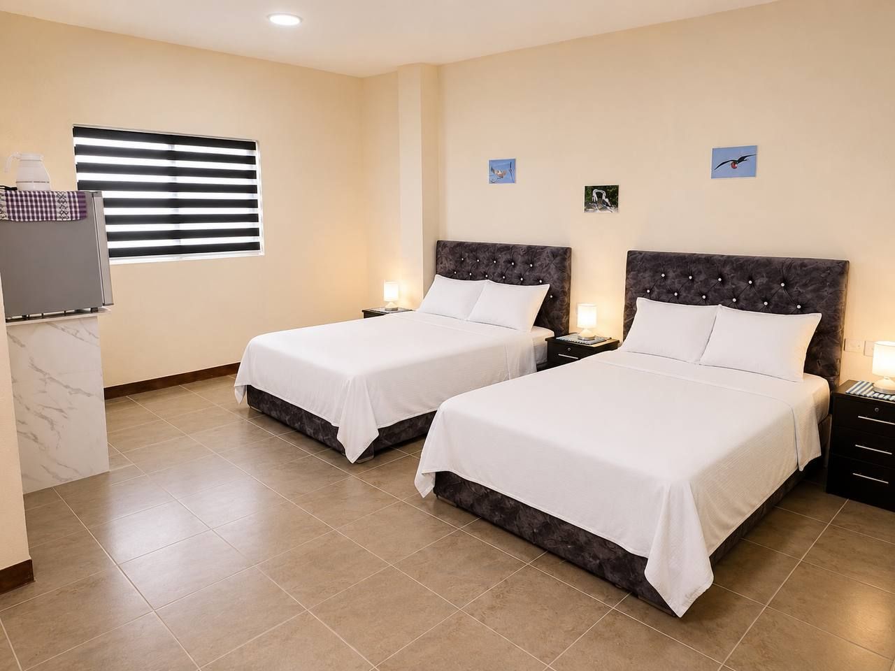 Habitación de hotel con dos camas, televisor, ventana con persianas y una pequeña obra de arte en la pared.
