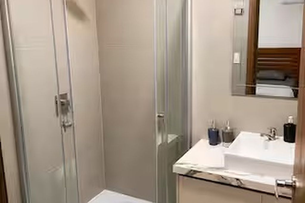 Un bagno moderno con cabina doccia in vetro, lavandino bianco e specchio sopra.
