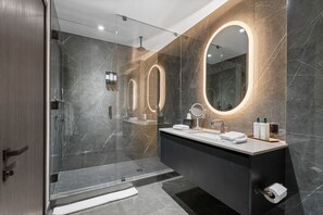 Un baño moderno con cabina de ducha de vidrio, tocador con espejo y pared revestida de mármol.