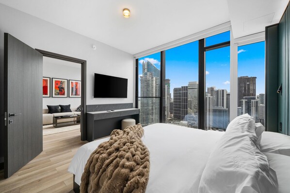 Habitación de hotel moderna con una cama grande, televisor de pantalla plana, vistas a la ciudad y una zona de estar acogedora con obras de arte.