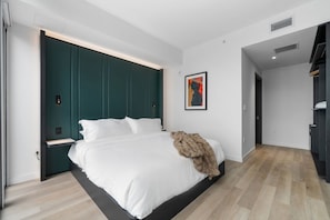 Ein modernes Schlafzimmer mit einem großen Bett, einer dunkelgrünen Kopfteil, einer weißen Wand und einem Holzboden.