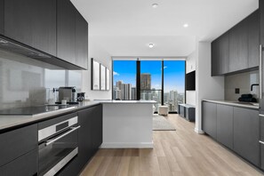 Een moderne keuken met donkere kastjes, een centraal eiland en een stadszicht door grote ramen.