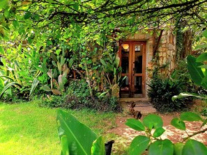 A rustic stone building with a wooden door, surrounded by dense greenery and a grassy area. - ​Spacious Garden Haven  Pet-Friendly & Great Loc. in San Cristóbal de las Casas (San Cristóbal de las Casas)