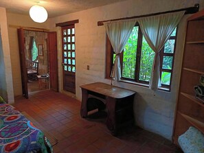 A room with a bed, a desk, a chair, a window with curtains, and a door with a view of greenery outside. - ​Spacious Garden Haven  Pet-Friendly & Great Loc. in San Cristóbal de las Casas (San Cristóbal de las Casas)