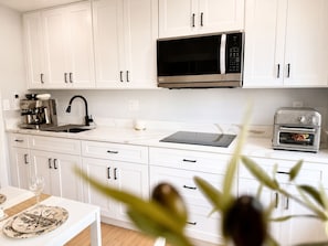 A modern kitchen with white cabinets, a black microwave, a coffee machine, and a toaster.