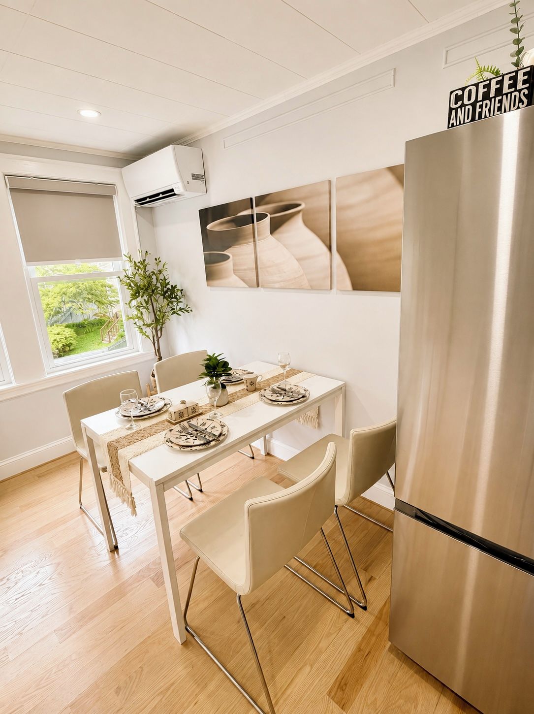 Comedor con una mesa blanca para cuatro, un refrigerador de acero inoxidable y un aire acondicionado instalado en la pared.