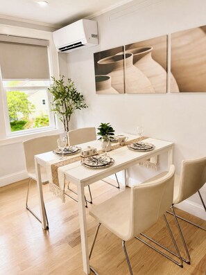 A dining area with a white table set for four, a potted plant, and artwork on the wall. - Newly Renovated 3BR Private Home in Newton (Newton)