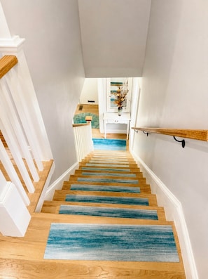 A staircase with wooden steps and blue carpeting leading to a landing with a white console table and a vase of dried flowers.