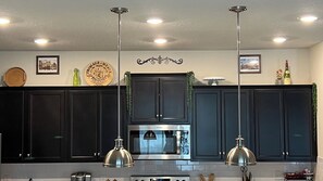 A kitchen with dark cabinets, stainless steel appliances, pendant lights, and decorative wall items. - Spacious 5-BR Disney themed townhome in Davenport, Windsor Island Resort (Davenport)