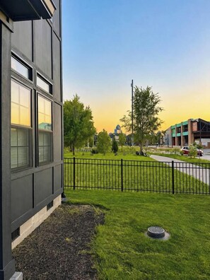 A modern building with large windows, a grassy yard, a metal fence, and a clear sky. - Brand New Modern Home, Steps to Bottleworks! (Indianapolis)