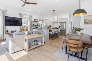 A modern living room with a sofa, coffee table, and TV. There is a kitchen area with a dining table and chairs. - Brand New Modern Home, Steps to Bottleworks! (Indianapolis)