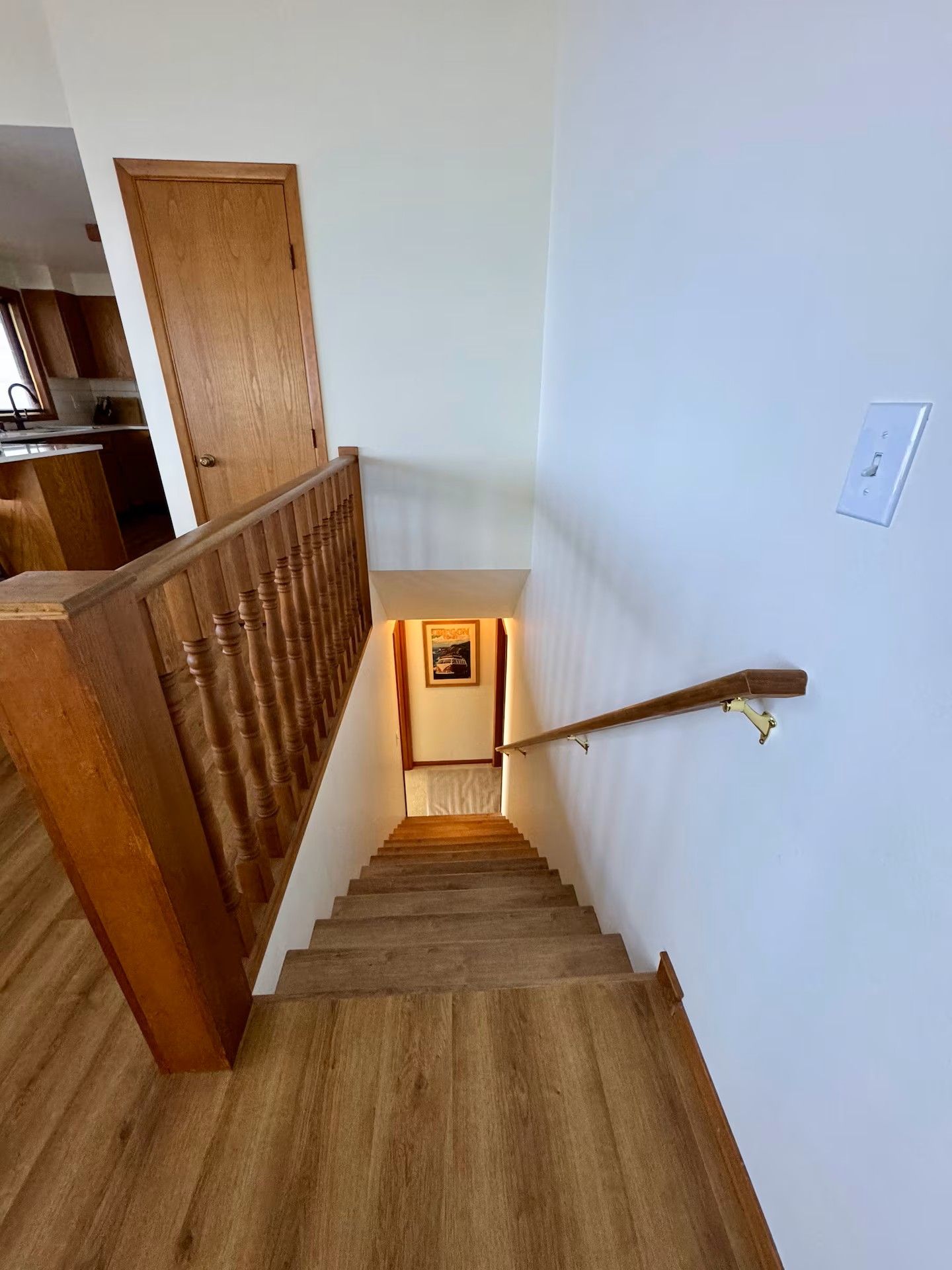 Un escalier en bois avec une rampe, menant à un palier où est accrochée une image encadrée.