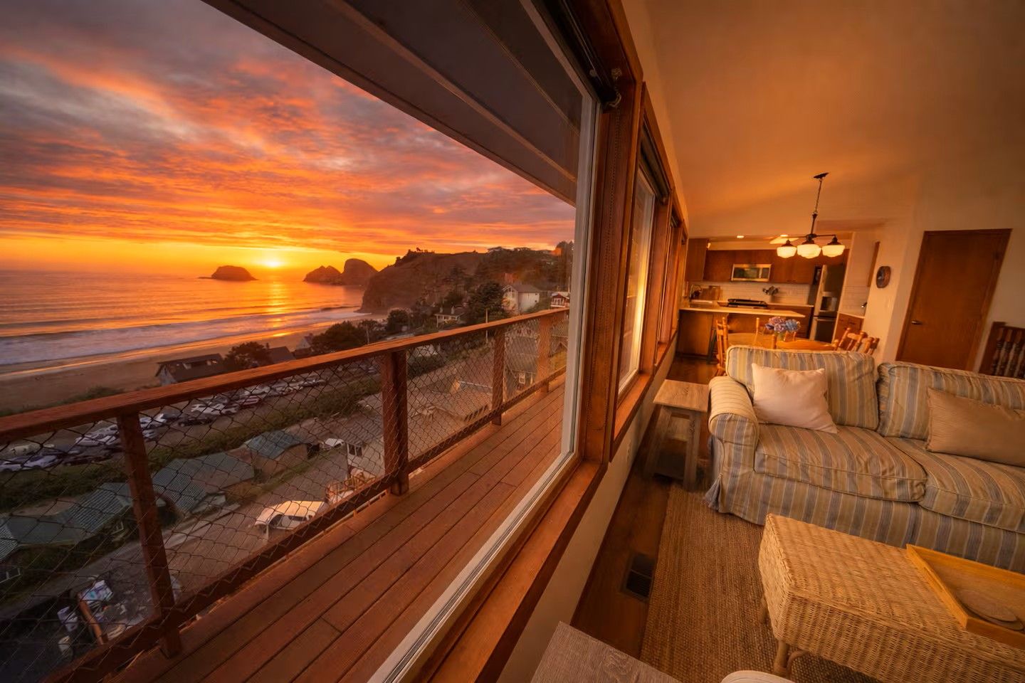 Una habitación con vista al océano al atardecer, una terraza de madera y un rincón de estar acogedor con un sofá y una mesita.