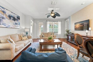 A living room with a sofa, a coffee table, a blue bean bag, a ceiling fan, and a painting on the wall. - Work, Play and Stay, 3BR, Prime Orlando Location (Orlando)