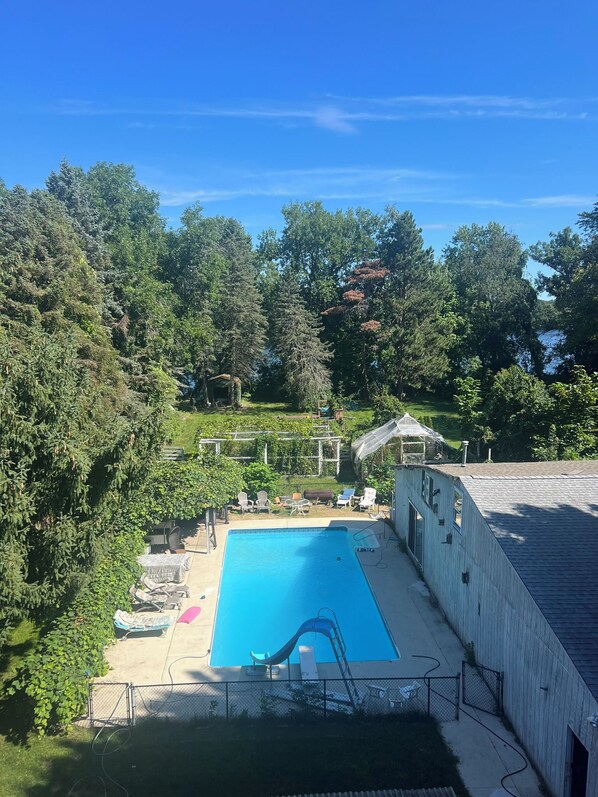 A swimming pool with a slide, surrounded by a fenced area, and a building with a sloped roof.