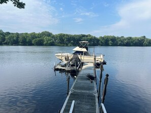 A boat docked at a pier with a calm lake and a forested shoreline in the background.