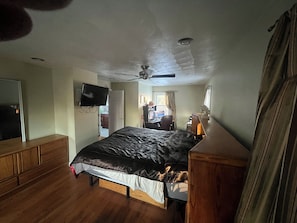 A bedroom with a bed, a desk, a chair, a television, and a ceiling fan.