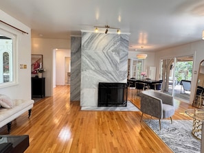 A modern living room with a fireplace, wooden flooring, and a dining area with a glass table.