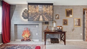 Quarto com lareira, uma grande moldura e uma mesa com objetos decorativos.