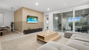 A modern living room with a flat-screen TV, a wooden coffee table, and a sofa. - 7BR Villa Solara Resort Pool & Cinema Near Disney (Kissimmee)