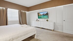 Quarto com cama, televisão na parede, penteadeira e porta.