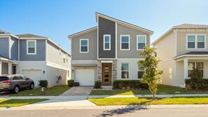A modern two-story residential building with a garage, a driveway, and a well-maintained lawn. - 7BR Villa Solara Resort Pool & Cinema Near Disney (Kissimmee)
