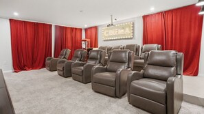 Sala de cinema com poltronas reclináveis, cortinas vermelhas e um letreiro luminoso com tema de cinema.