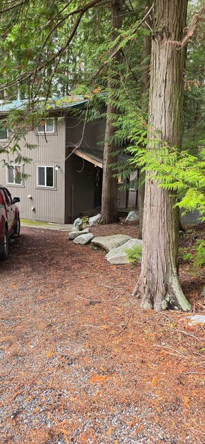 Een chalet met een overdekte veranda, omgeven door bomen en een grindpad.