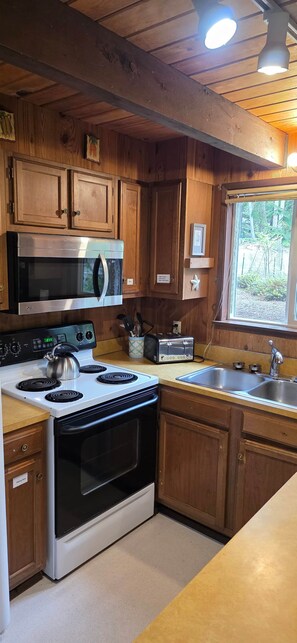 A kitchen with wooden cabinets, a stainless steel stove, a microwave, and a sink. - The Chalet on Lopez: it's peaceful! (Lopez Island)