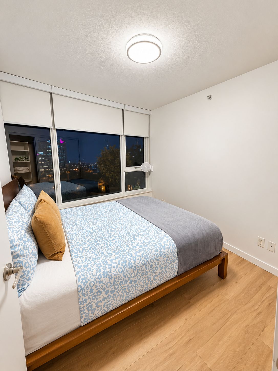 A bedroom with a bed, a window, and a view of a cityscape at night.