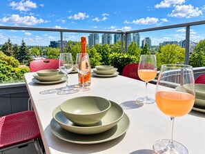 A table set for dining with a bottle of wine, glasses, and bowls, overlooking a cityscape. - 2BR+Sofabed, 2Bath, Private 500sqft sundeck, EV Parking w/Pool, Sauna, Hot Tub (Vancouver)