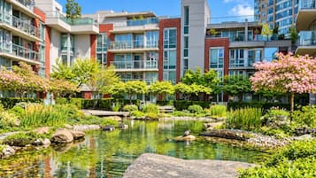 A modern residential building with a landscaped garden featuring a pond and various plants.