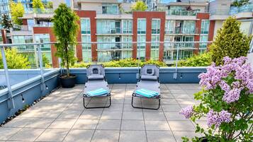 A rooftop terrace with two sun loungers, potted plants, and a view of high-rise buildings.