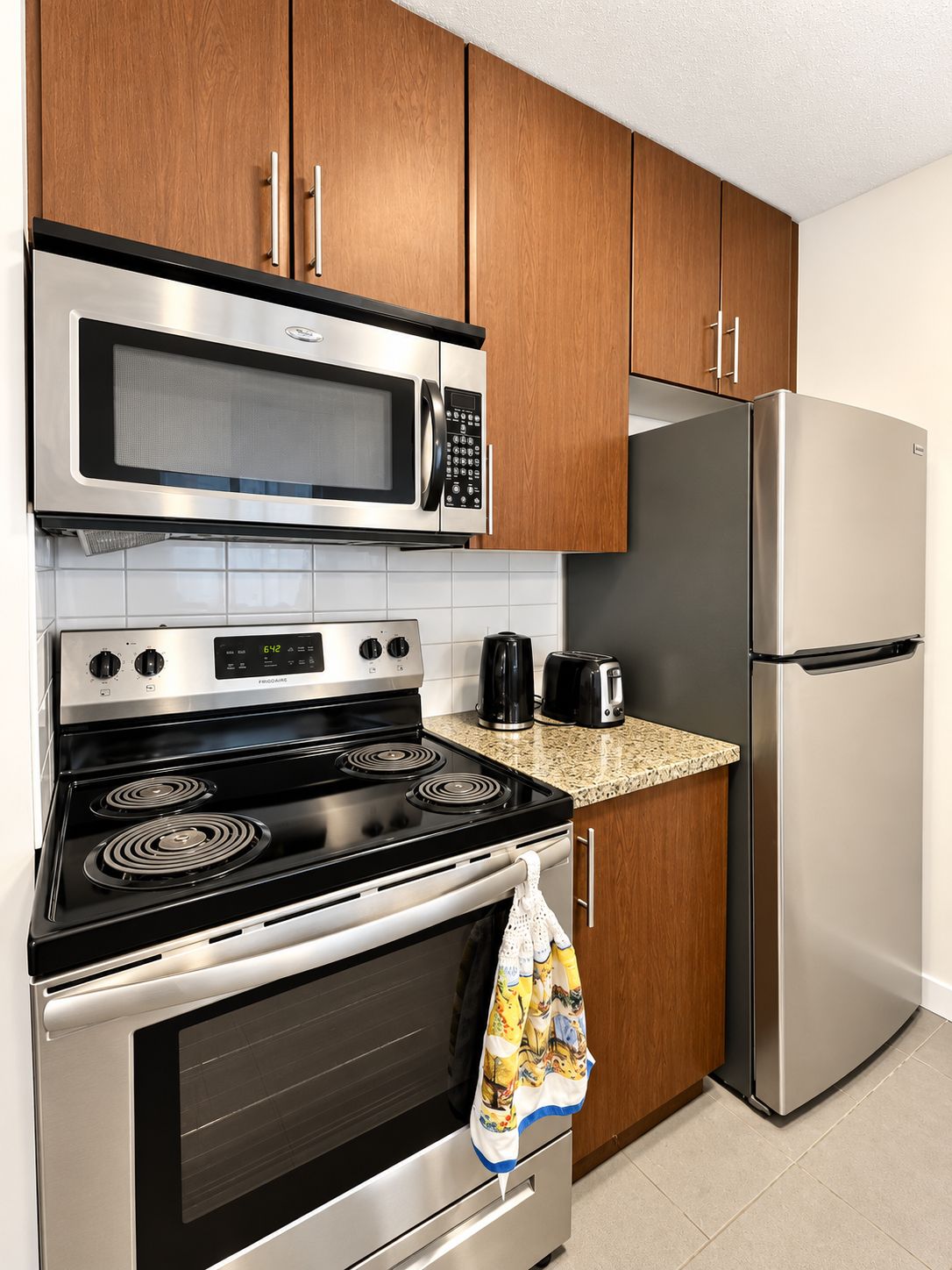 A kitchen with a stainless steel microwave, a stove, a refrigerator, and wooden cabinets.