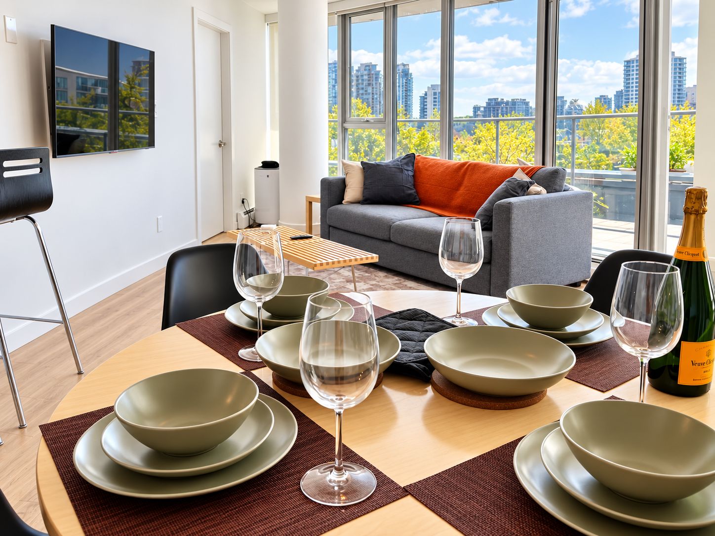 A modern living room with a dining area, a sofa with orange cushions, and a large window with a city view.