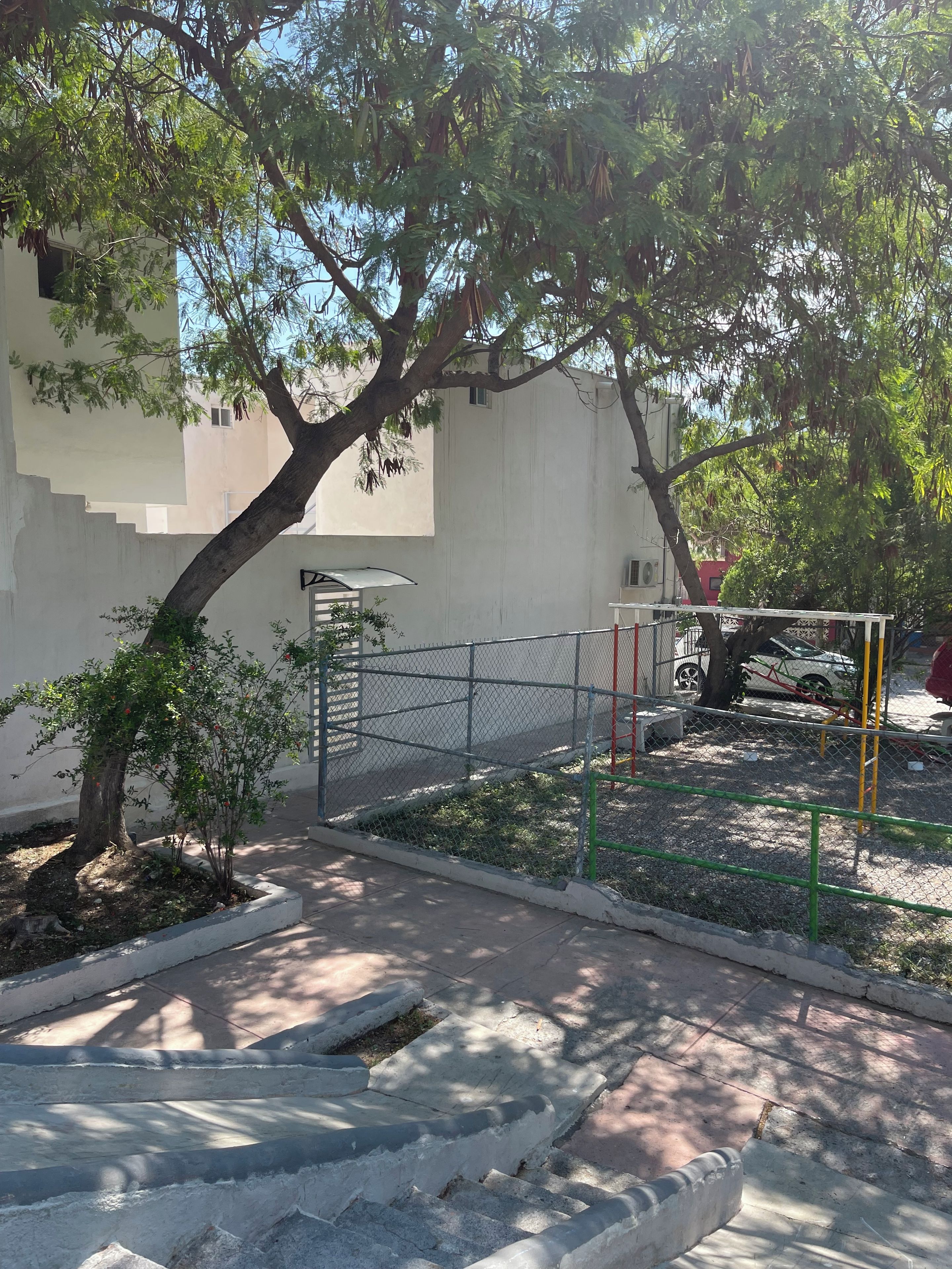 Un camino pavimentado que conduce a una zona vallada con un parque infantil.
