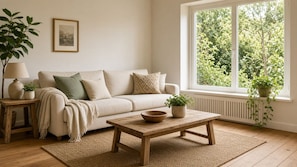 A cozy living room with a beige sofa, a wooden coffee table, a lamp, and a view of greenery through a window. - Peaceful Luxury Pad (Ascot Vale)