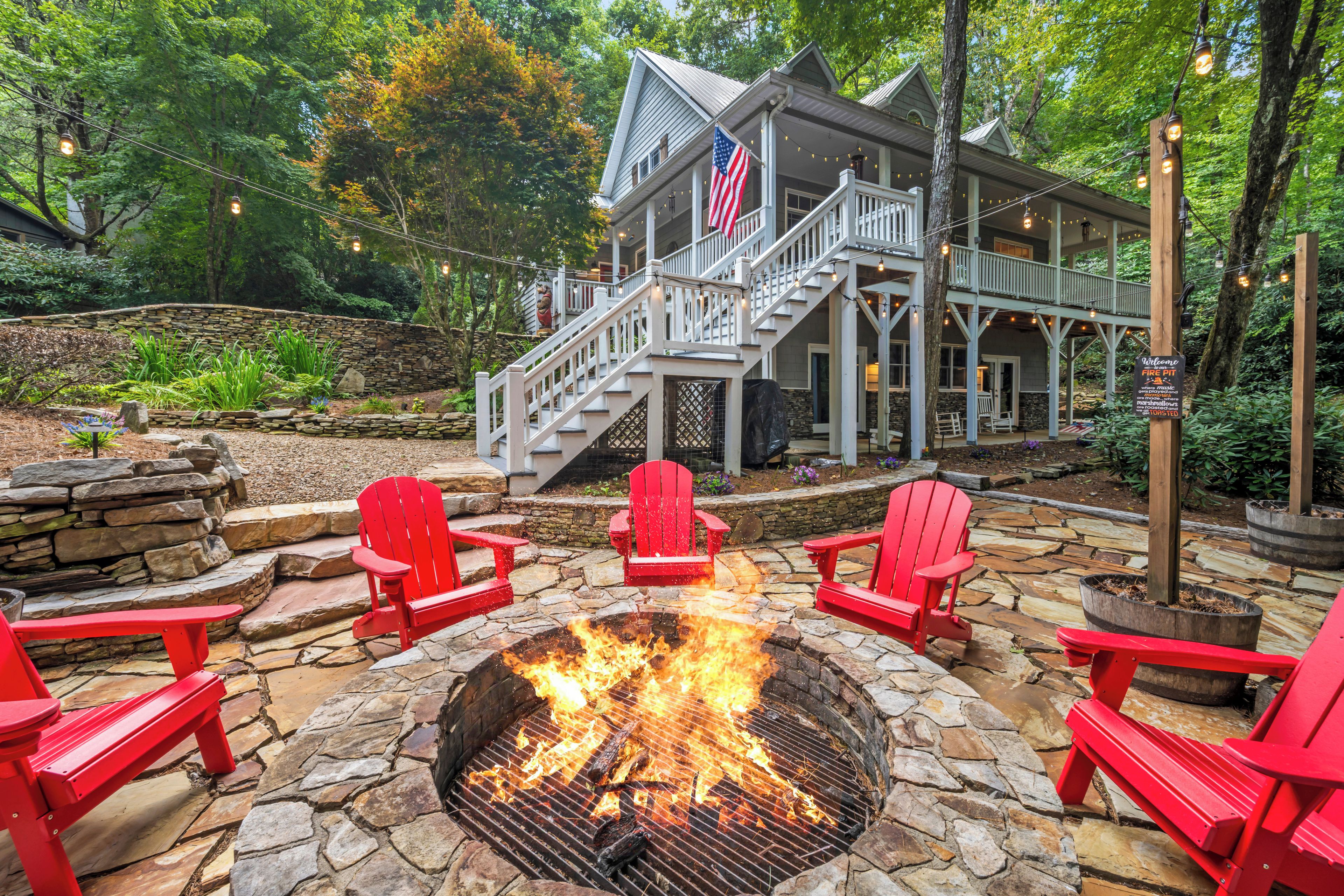A stone fire pit with red Adirondack chairs in a landscaped outdoor area.