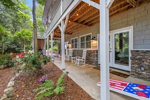 A covered outdoor patio with a stone wall, wooden beams, and a seating area with chairs and a table. - ** NEW RENTAL** Highlands Heaven | Walk to Town | Game Room | Firepit & Waterfall (Highlands)