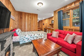 A cozy room with a red sofa, a wooden coffee table, a fireplace, and a television mounted on the wall. - ** NEW RENTAL** Highlands Heaven | Walk to Town | Game Room | Firepit & Waterfall (Highlands)