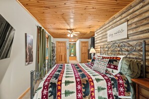 A bedroom with a wooden ceiling, a bed with a patterned blanket, a wall-mounted sign, and a window with curtains. - ** NEW RENTAL** Highlands Heaven | Walk to Town | Game Room | Firepit & Waterfall (Highlands)