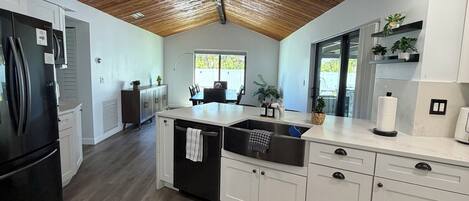 A modern kitchen with a wooden ceiling, white cabinetry, a black refrigerator, and a large window.
