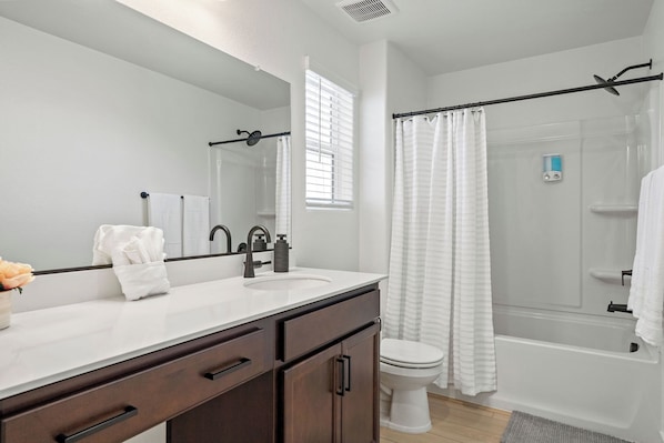 Un baño moderno con un lavamanos blanco, muebles oscuros, un inodoro y una zona de ducha.