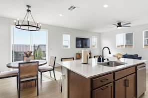A modern kitchen with a central island, dining area with chairs, a ceiling fan, and a TV mounted on the wall.