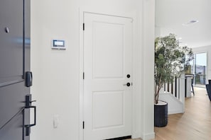 A modern interior with a white door, a digital lock, and a potted plant.