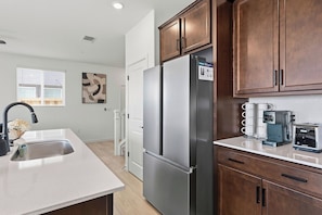 A modern kitchen with stainless steel appliances, wooden cabinets, and a countertop with coffee makers. - Sunset Haven Rocklin.
Brand-New Home with Stunning Sunset Views (Rocklin)