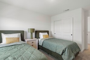 A bedroom with two single beds, a nightstand with a lamp, and a white door.