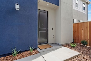 A modern house with a dark blue exterior, a wooden fence, and a concrete pathway leading to a door.
